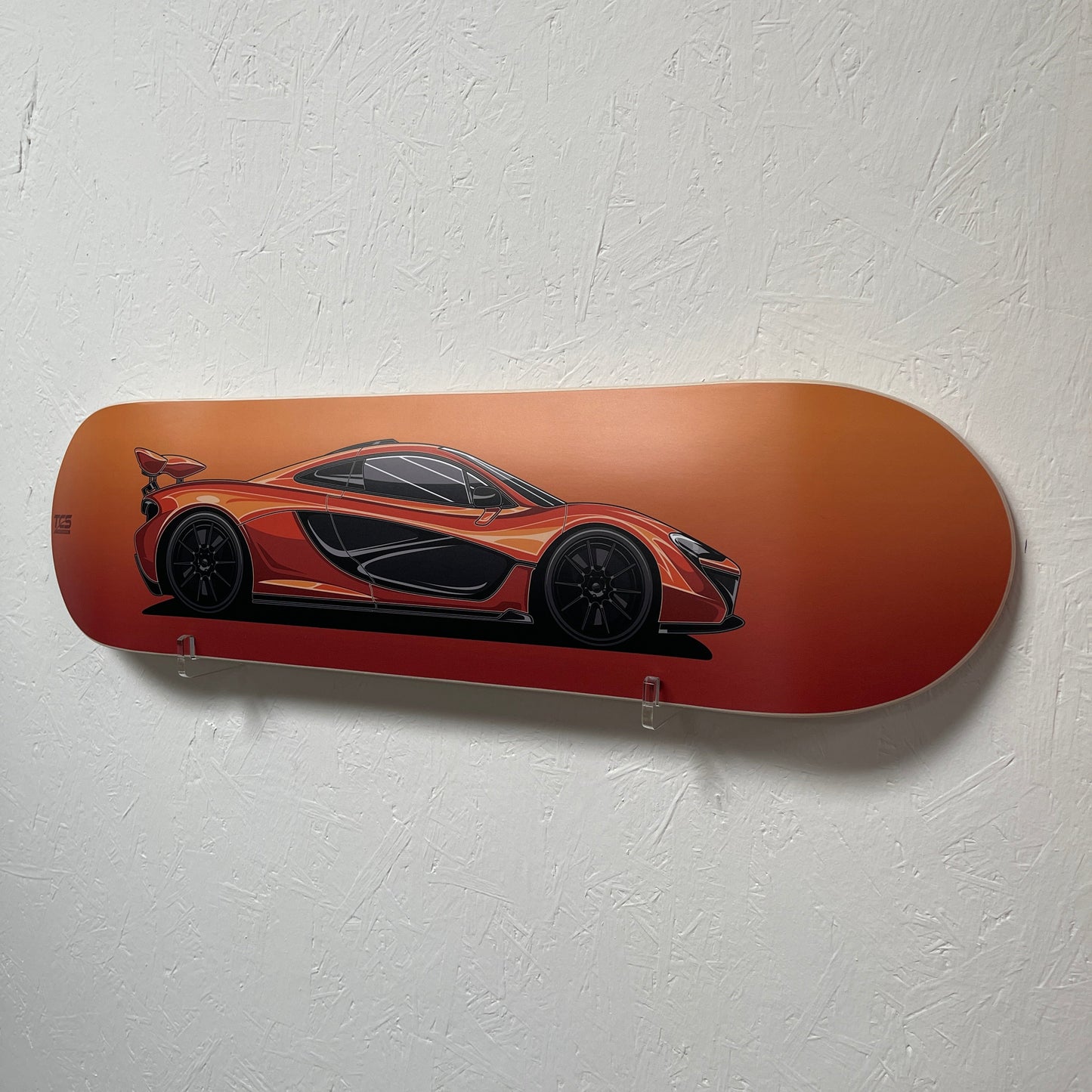 Orange skateboard deck with a black car design on a white wall