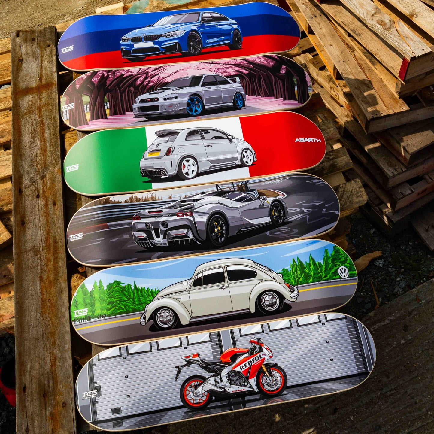 Skateboard decks with car and motorcycle designs on a wooden pallet.