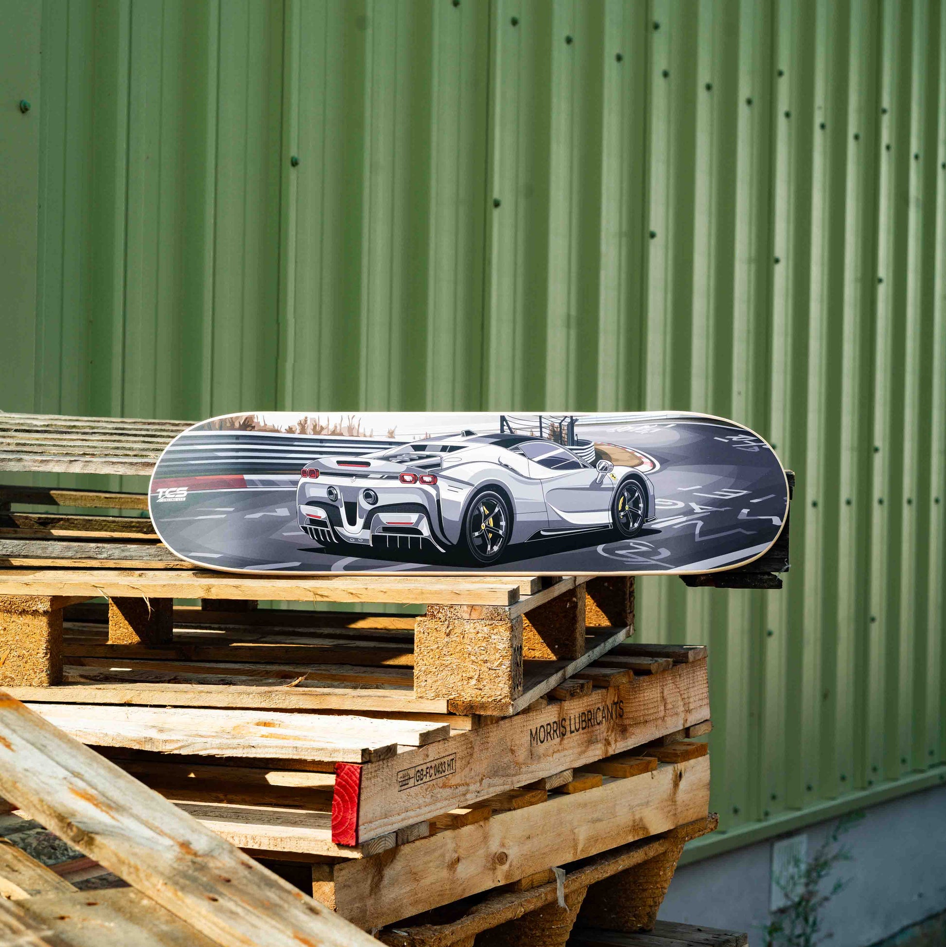 Skateboard with a car design on top of wooden pallets against a green wall.