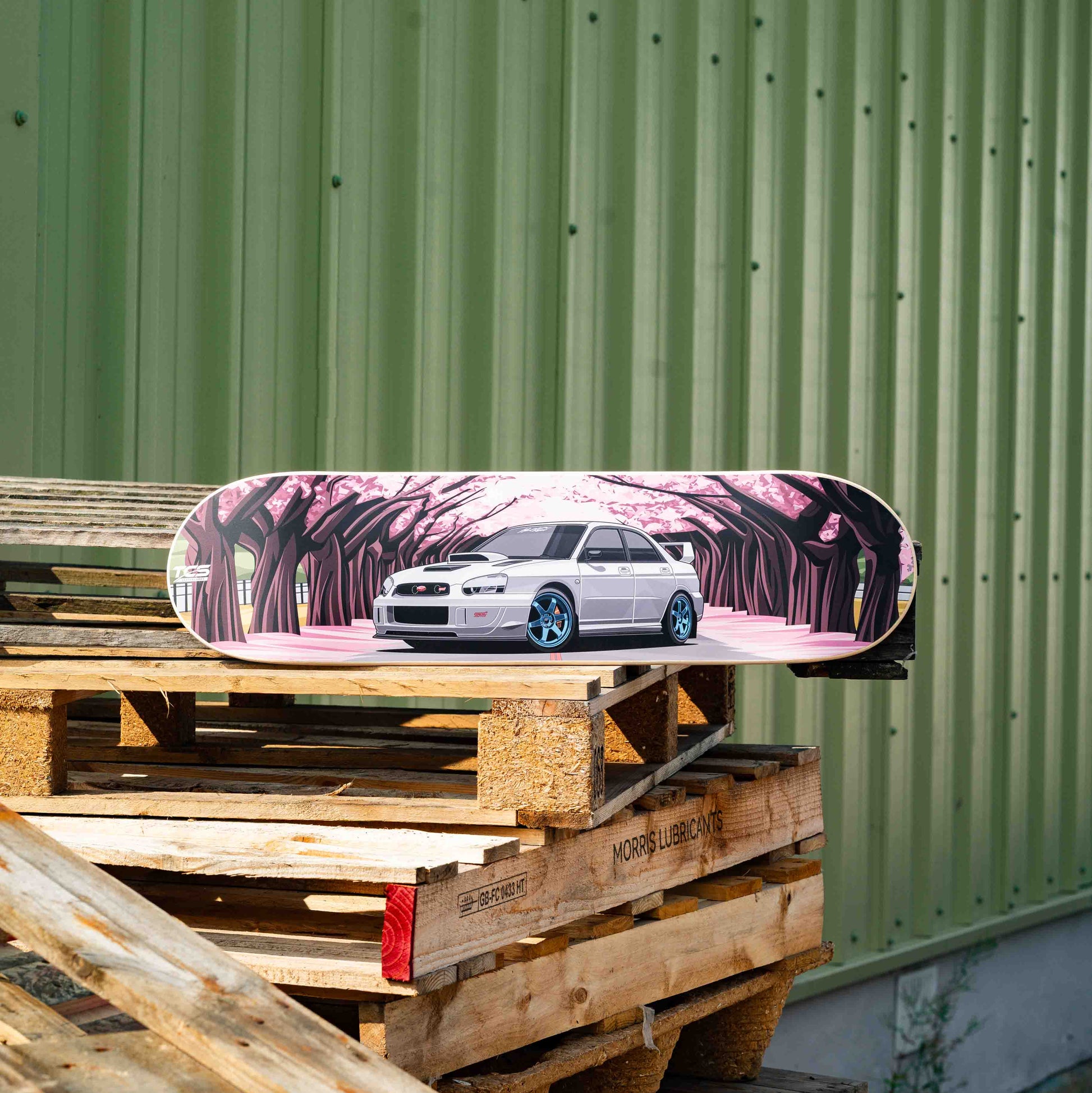 Skateboard with a car design on top of wooden pallets against a green wall.