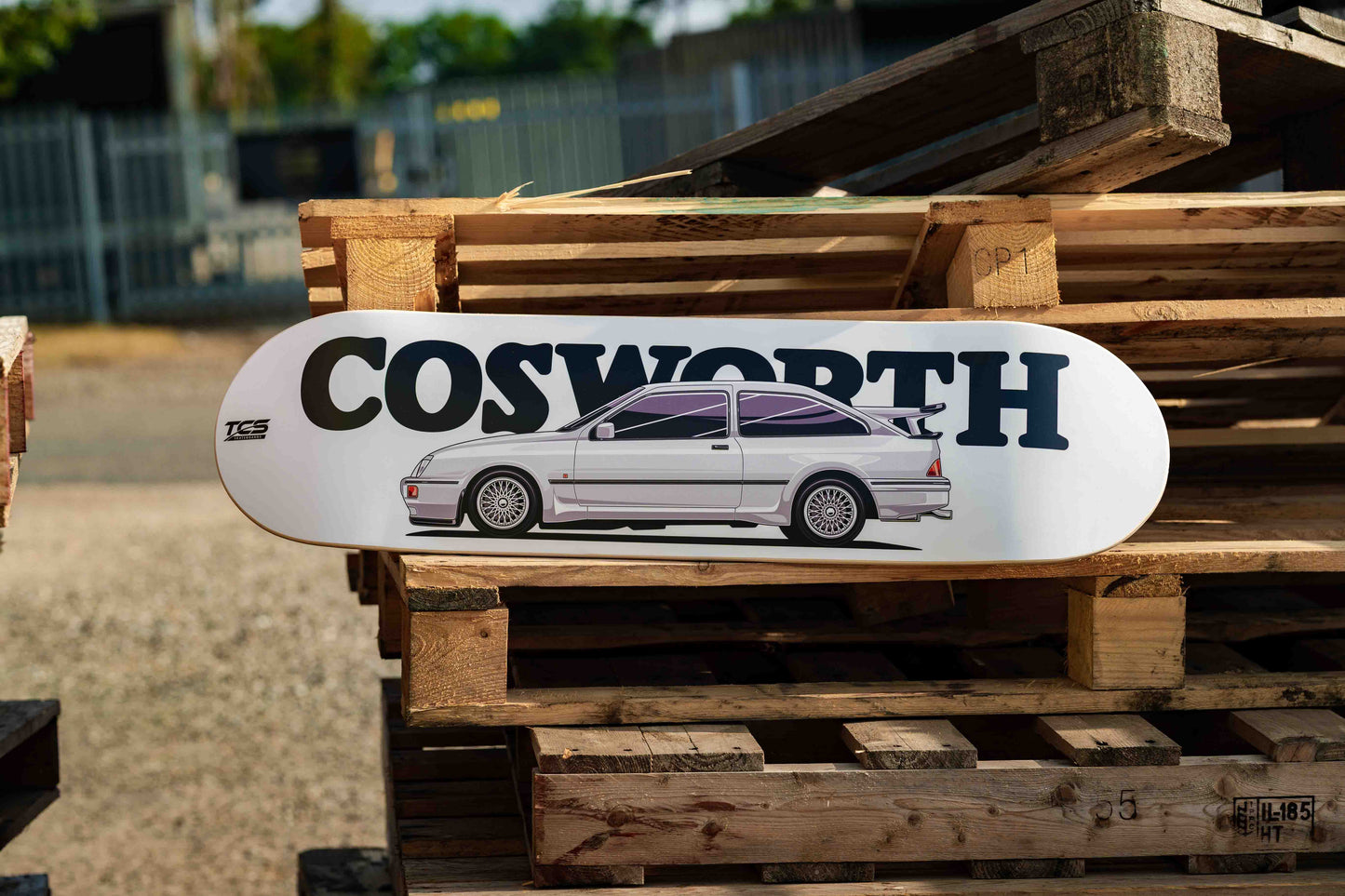 Skateboard with Cosworth logo and car illustration on a wooden pallet