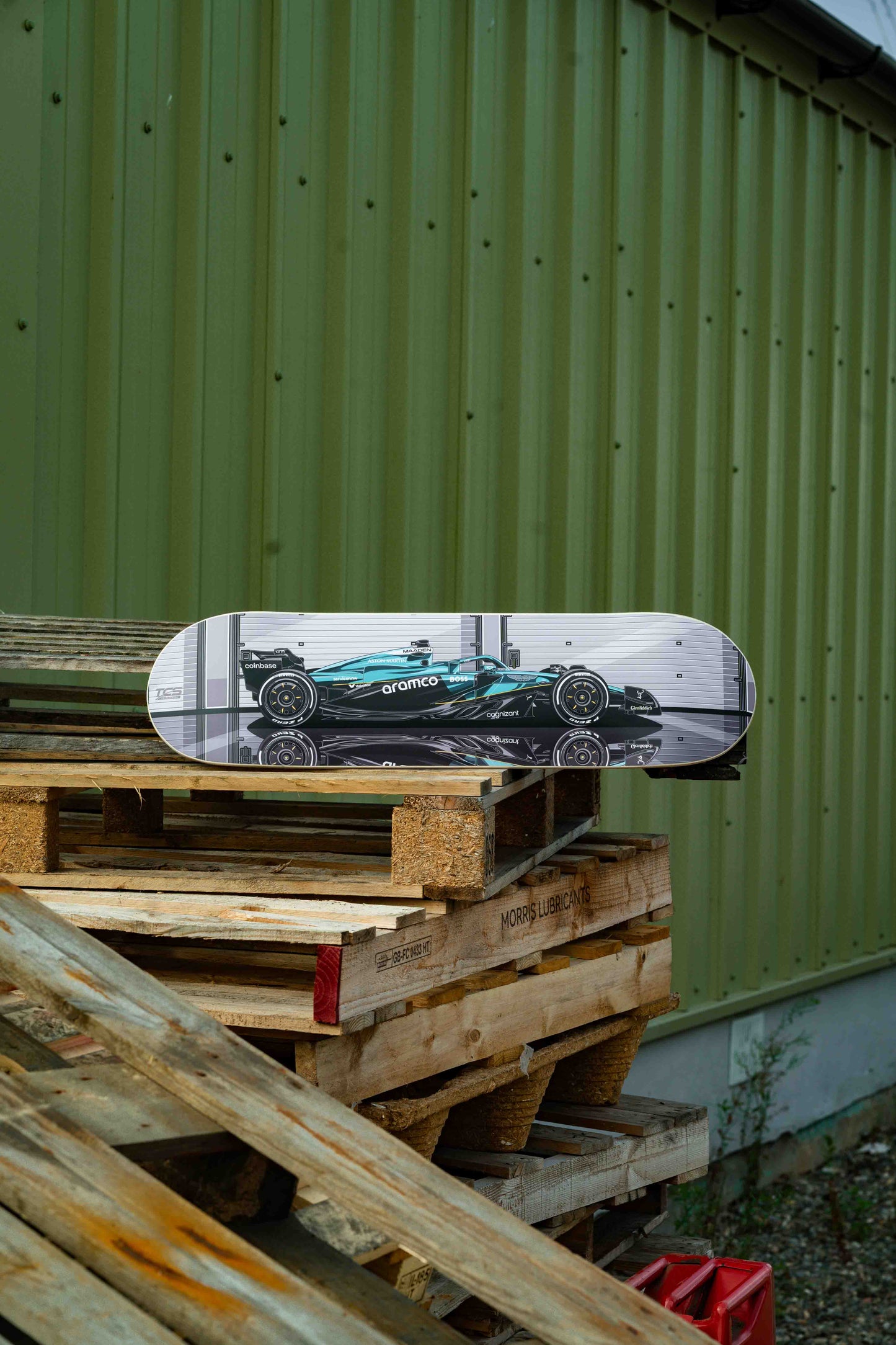 Skateboard with a car design on top of wooden pallets against a green wall.