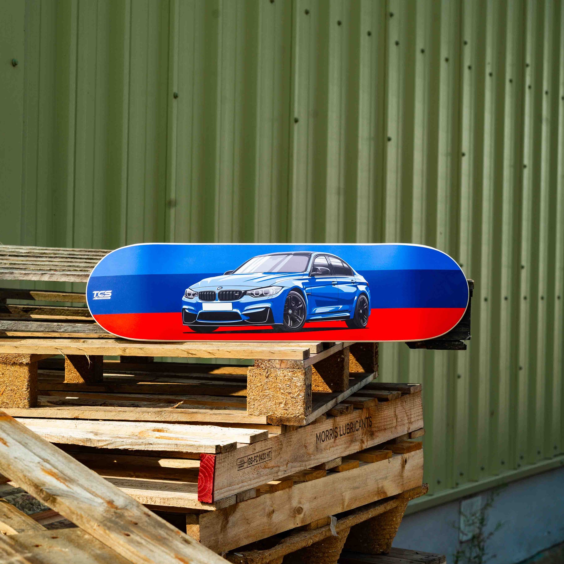 Skateboard with car design on a wooden pallet against a green wall.