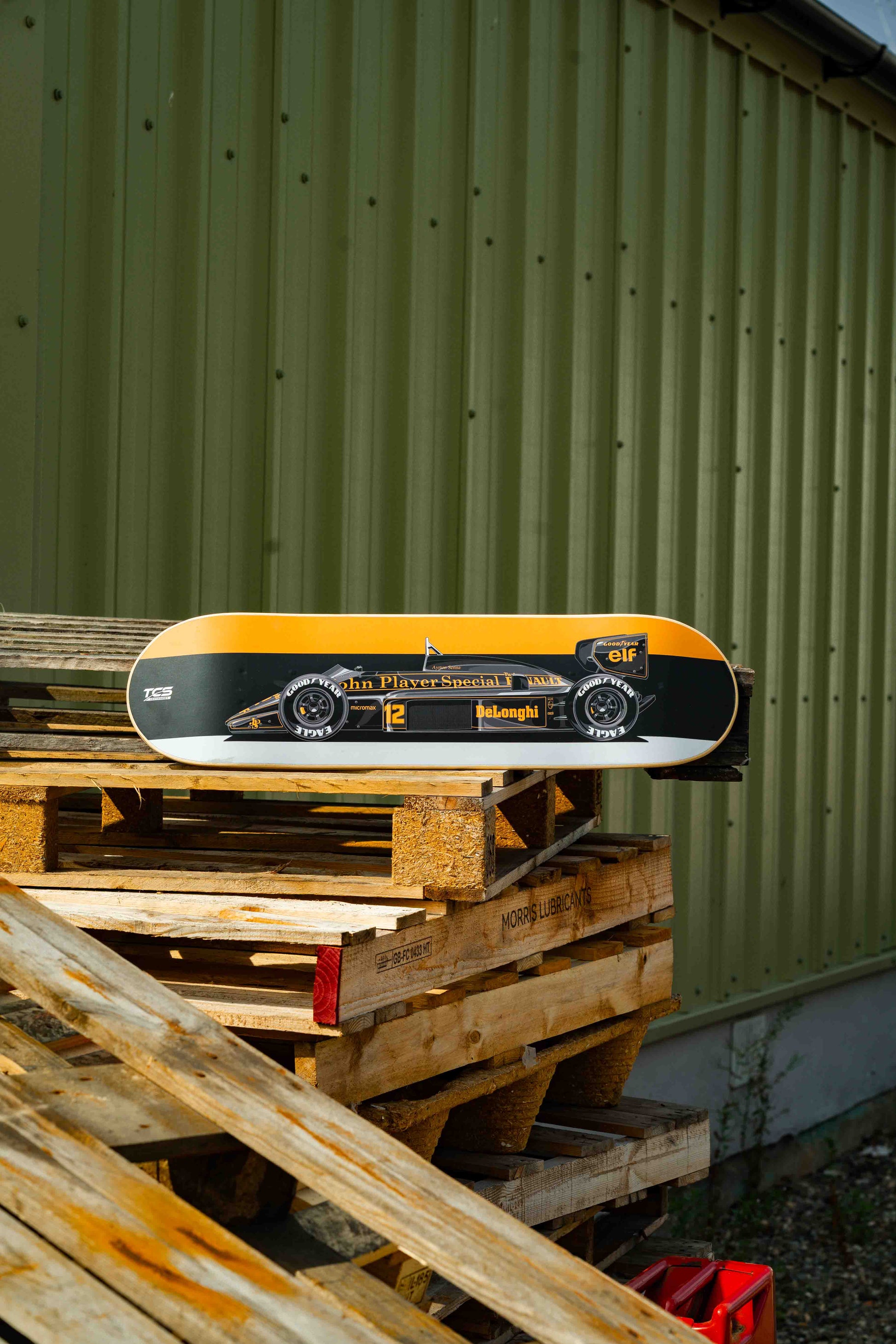 Skateboard with a black and yellow design on wooden pallets against a green wall.