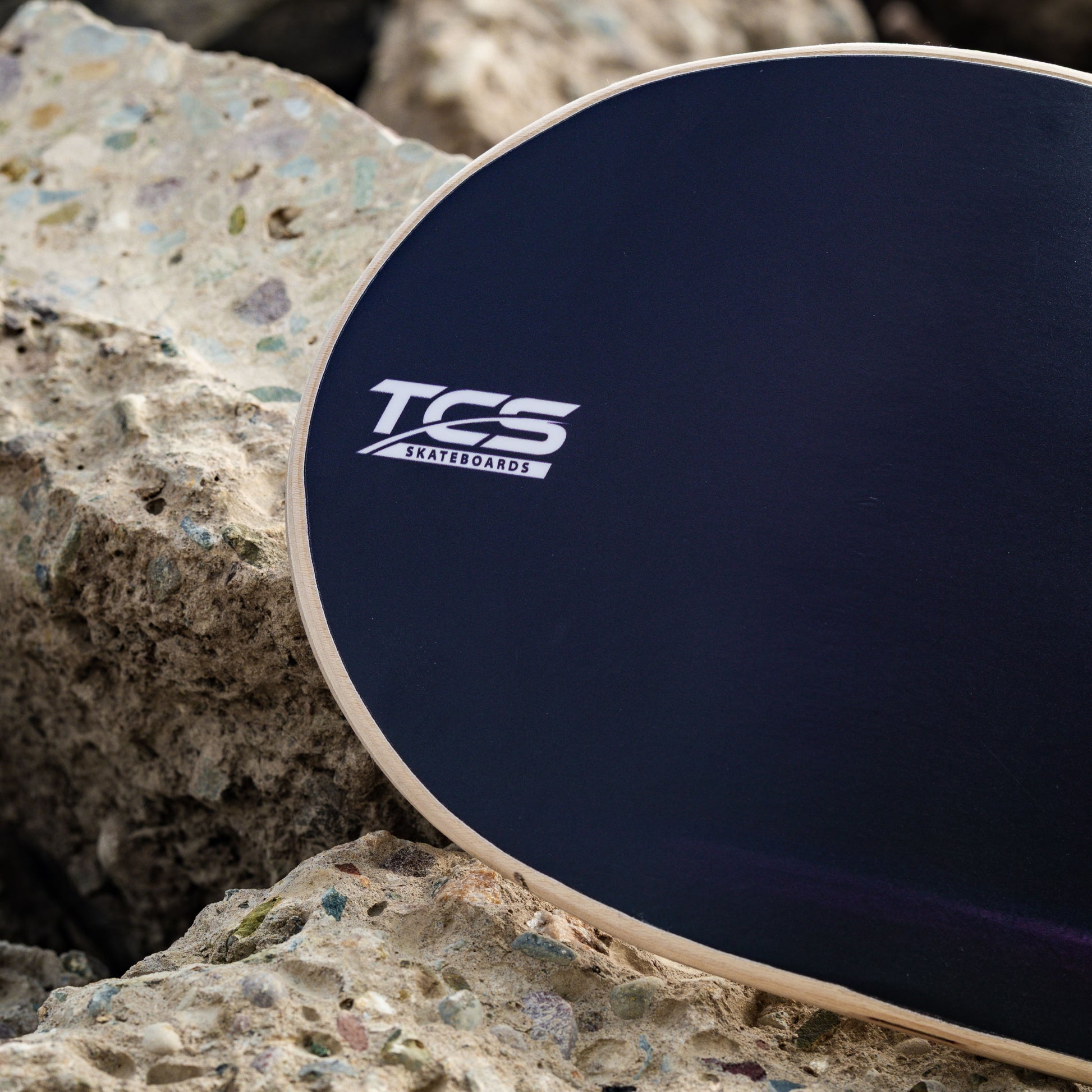 Black TCS skateboard deck on a rocky surface