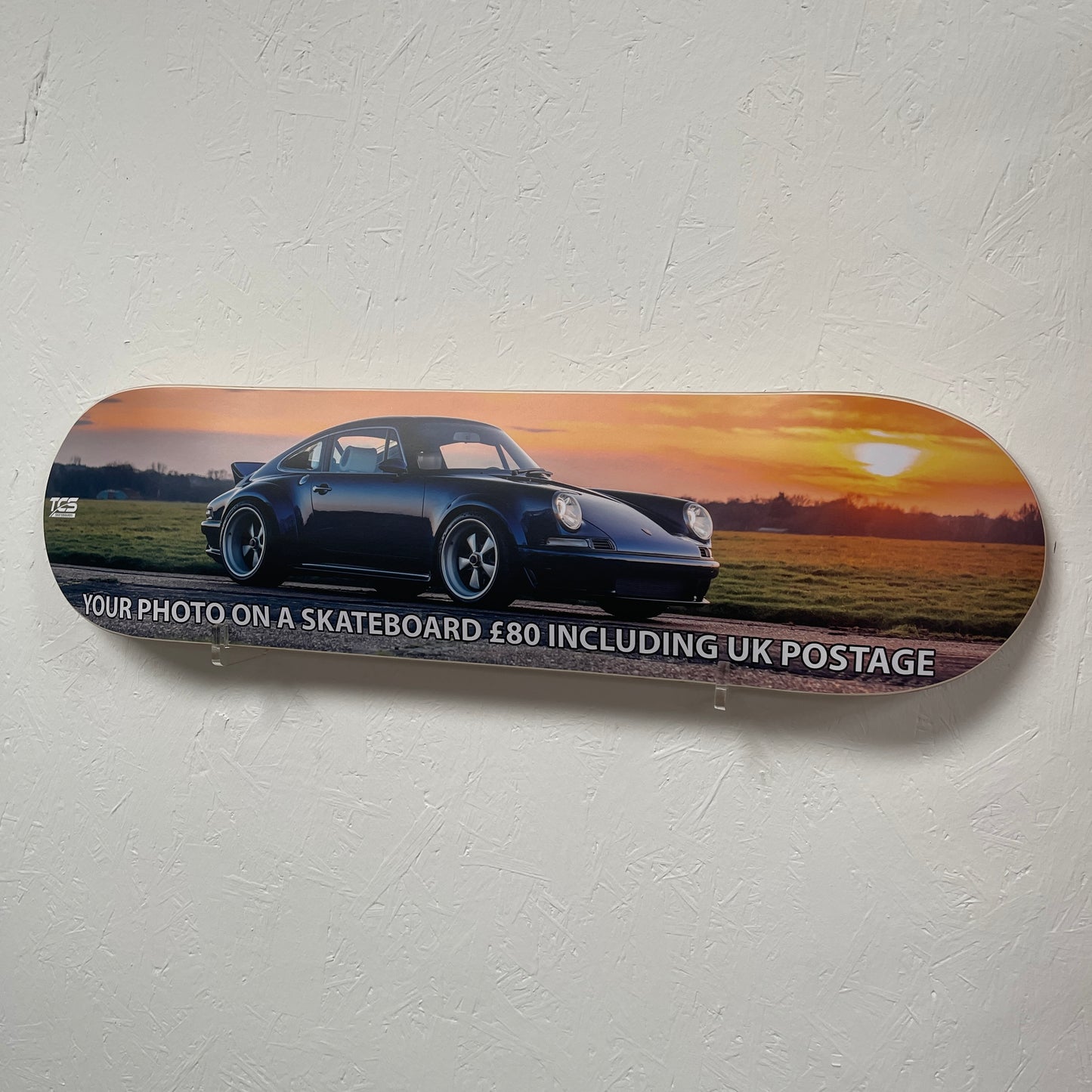 Skateboard deck with a car design and promotional text on a gray background
