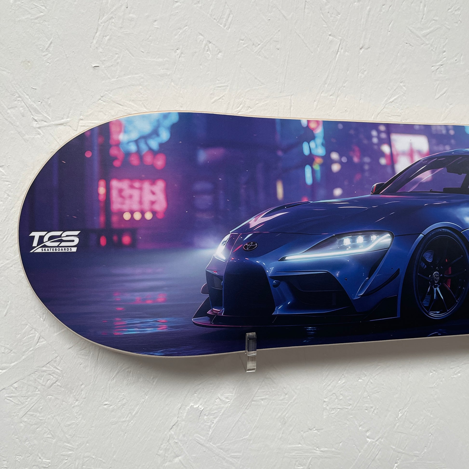 Skateboard deck with a car design and TCS branding on a white wall.
