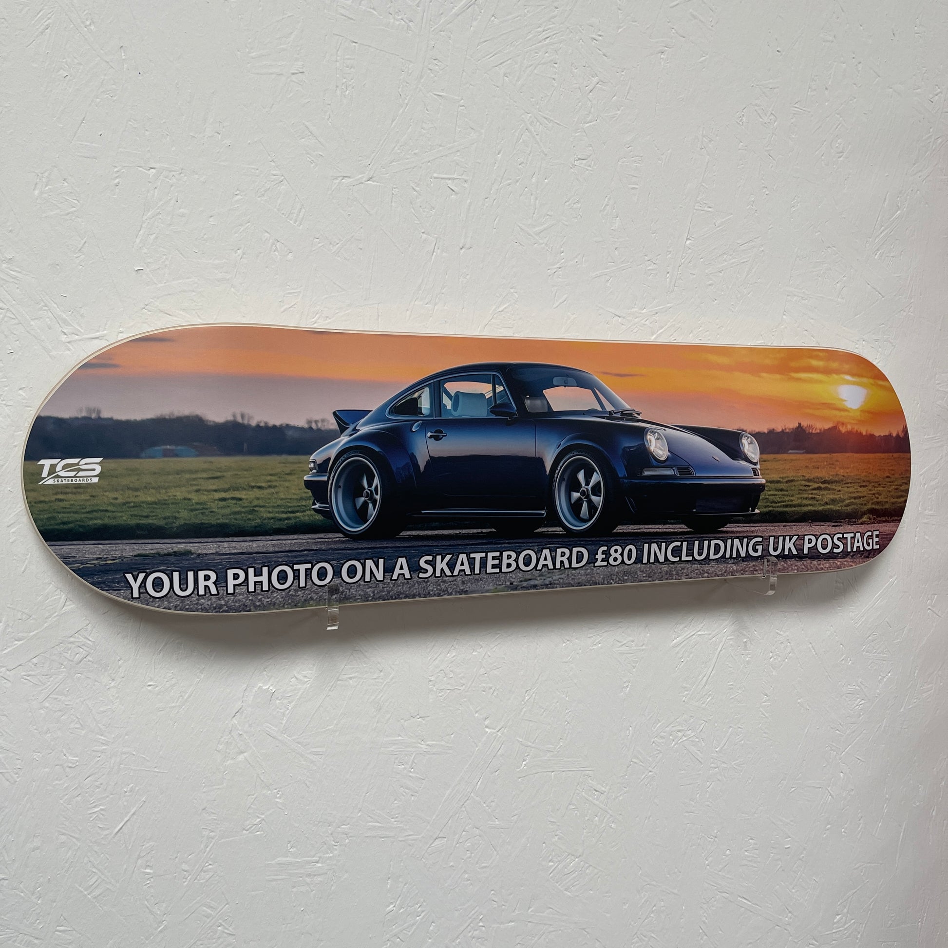 Skateboard deck with a car on a sunset background and promotional text.