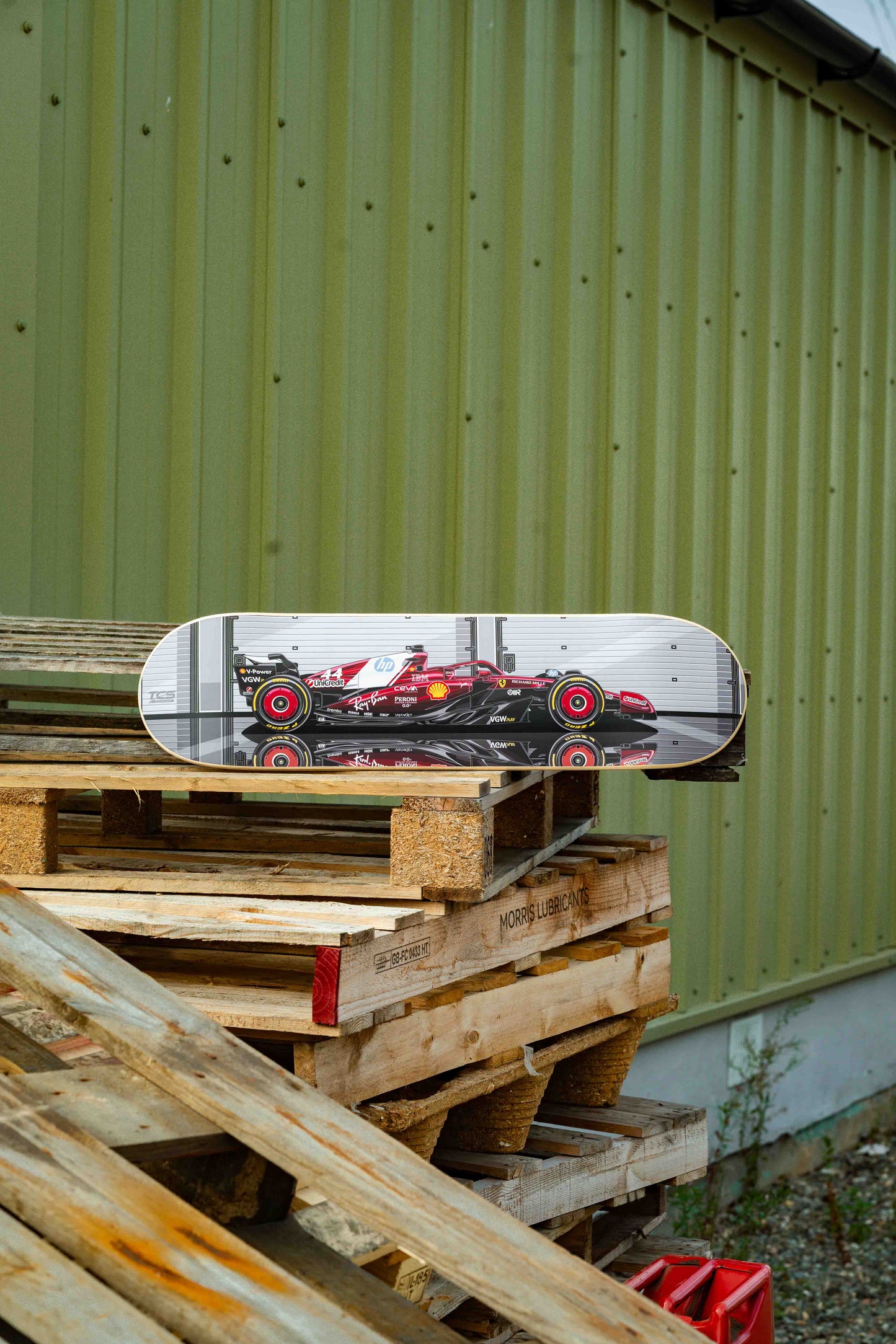 Skateboard with racing car design on a stack of wooden pallets against a green wall.