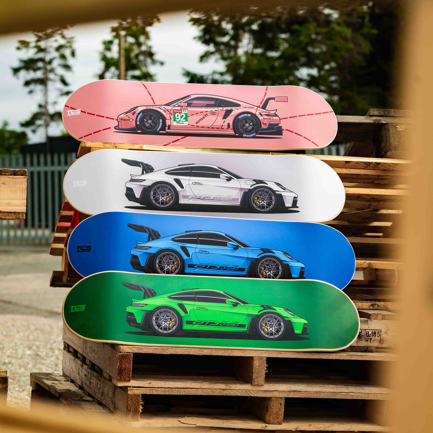 Four skateboard decks with car designs stacked on a wooden pallet.