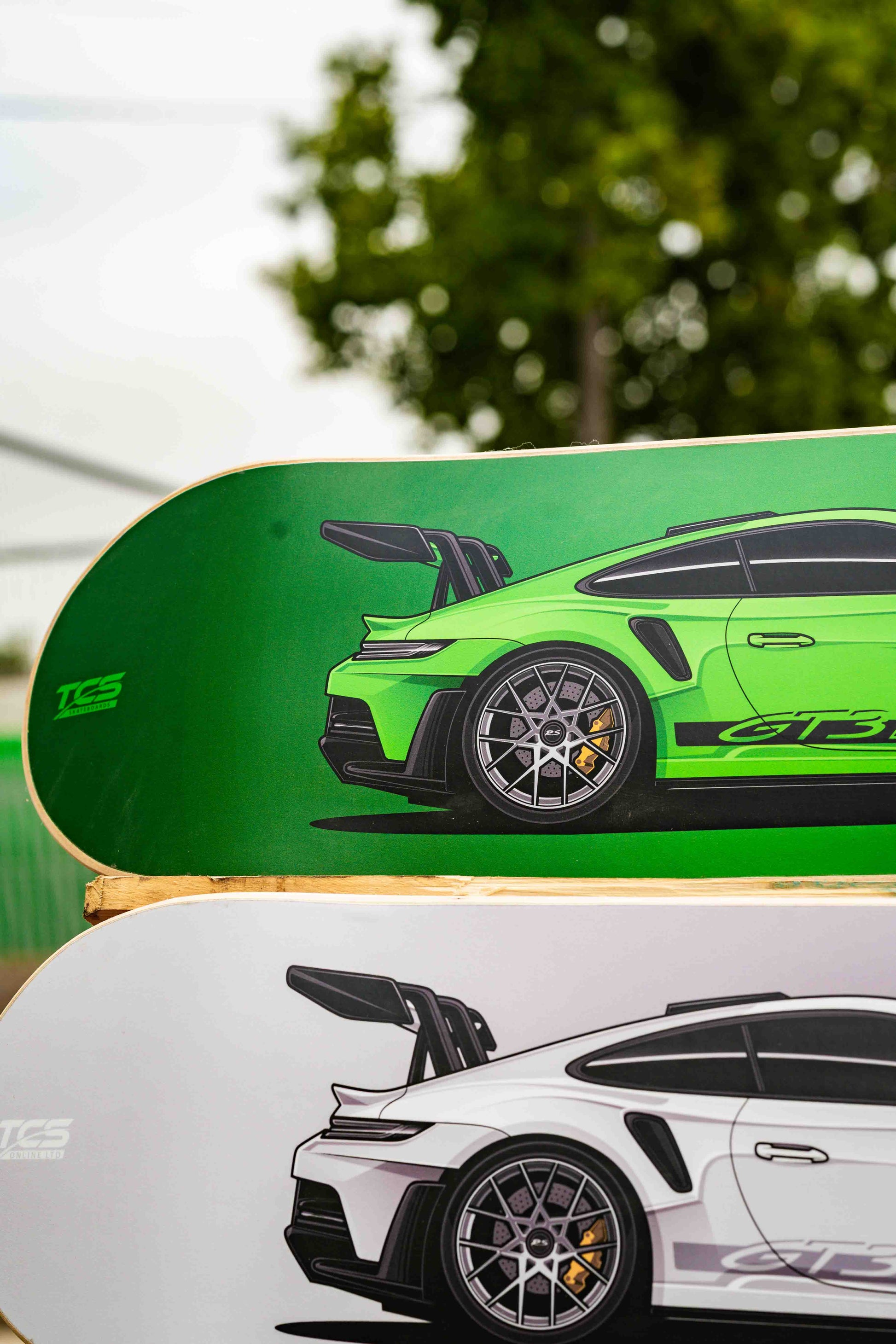 Two skateboard decks with car graphics on a blurred outdoor background