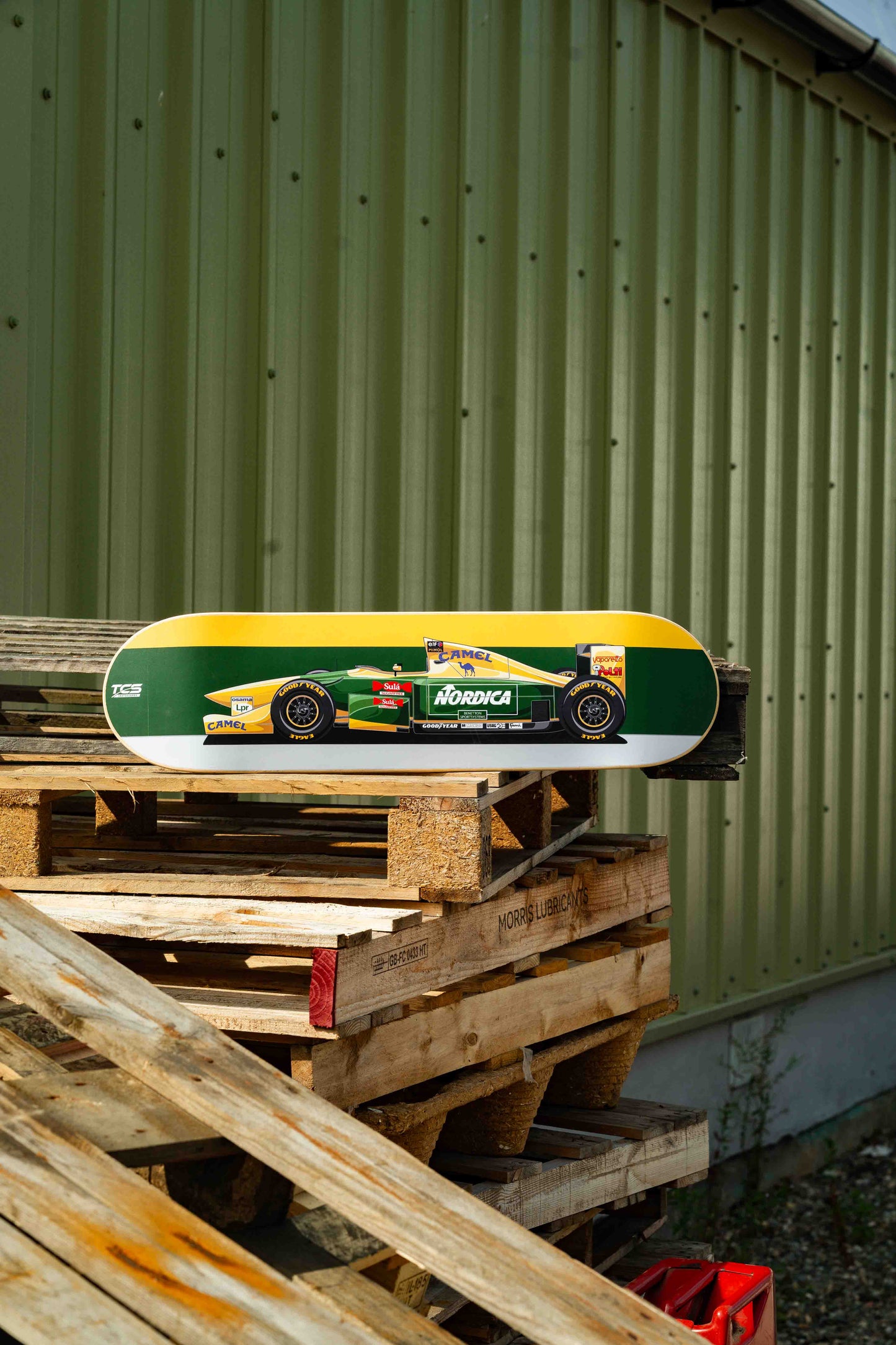 Skateboard with a racing car design on wooden pallets against a green wall.