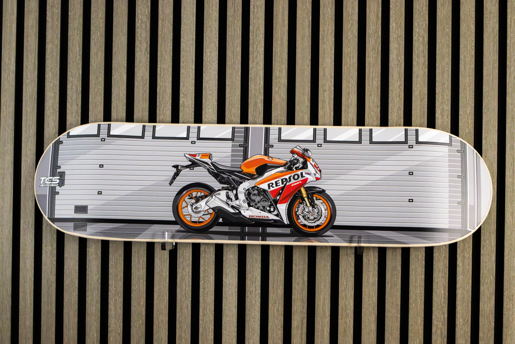 A skateboard deck featuring a graphic print of a Honda Repsol racing motorcycle, displayed flat against a vertical wood slat wall.
