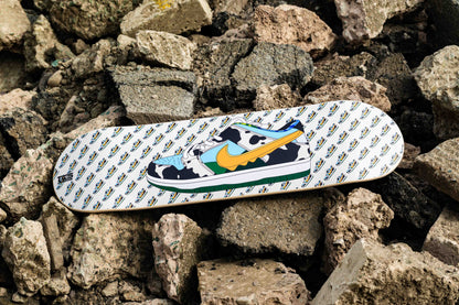 Skateboard deck with cow print design on a rocky surface