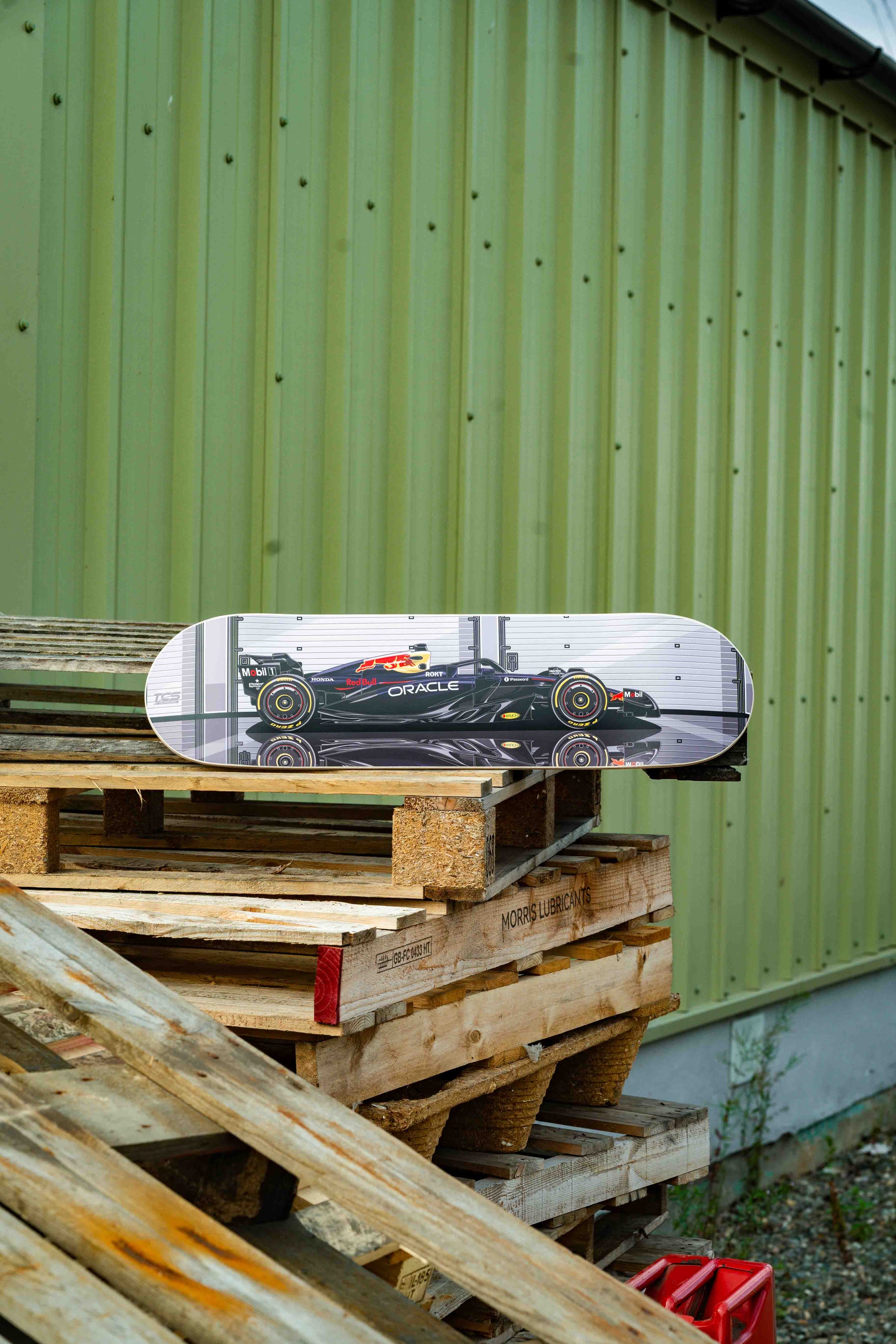 Skateboard with a car design on a wooden pallet against a green wall.