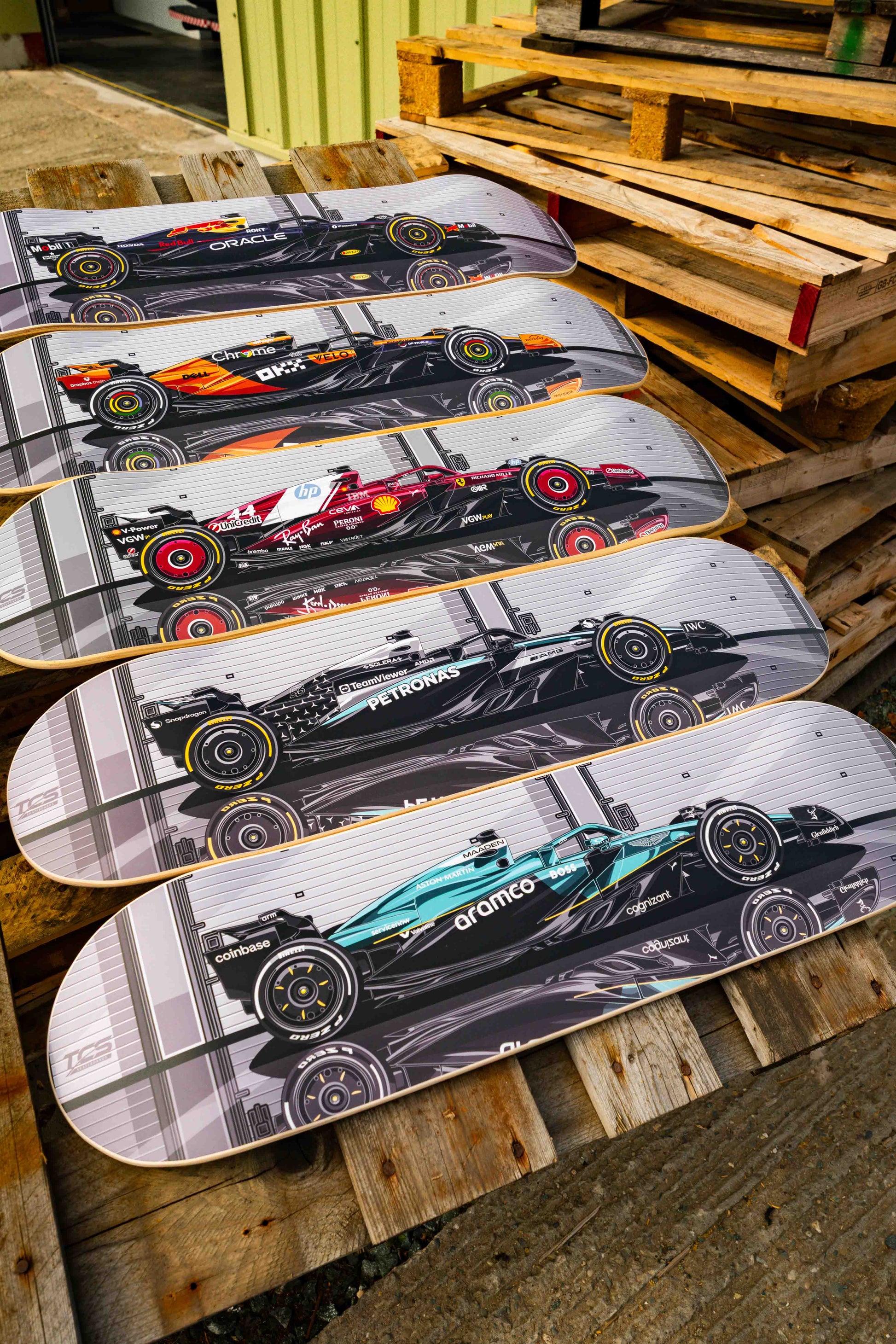 Five skateboard decks with Formula 1 car designs on a wooden pallet.
