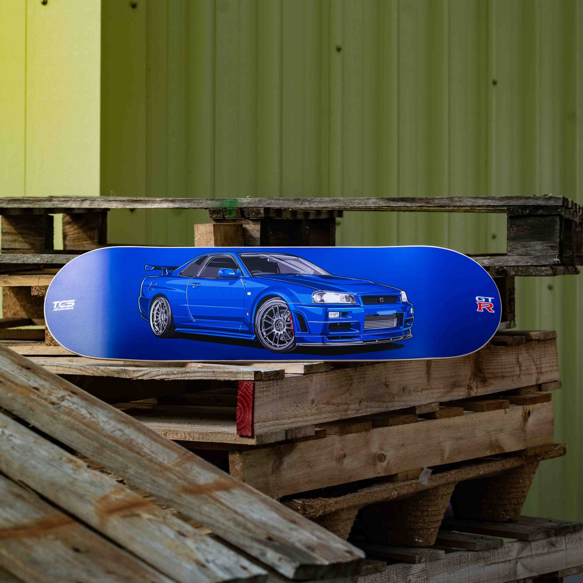 Blue car-shaped object on wooden pallets with a green corrugated metal wall in the background