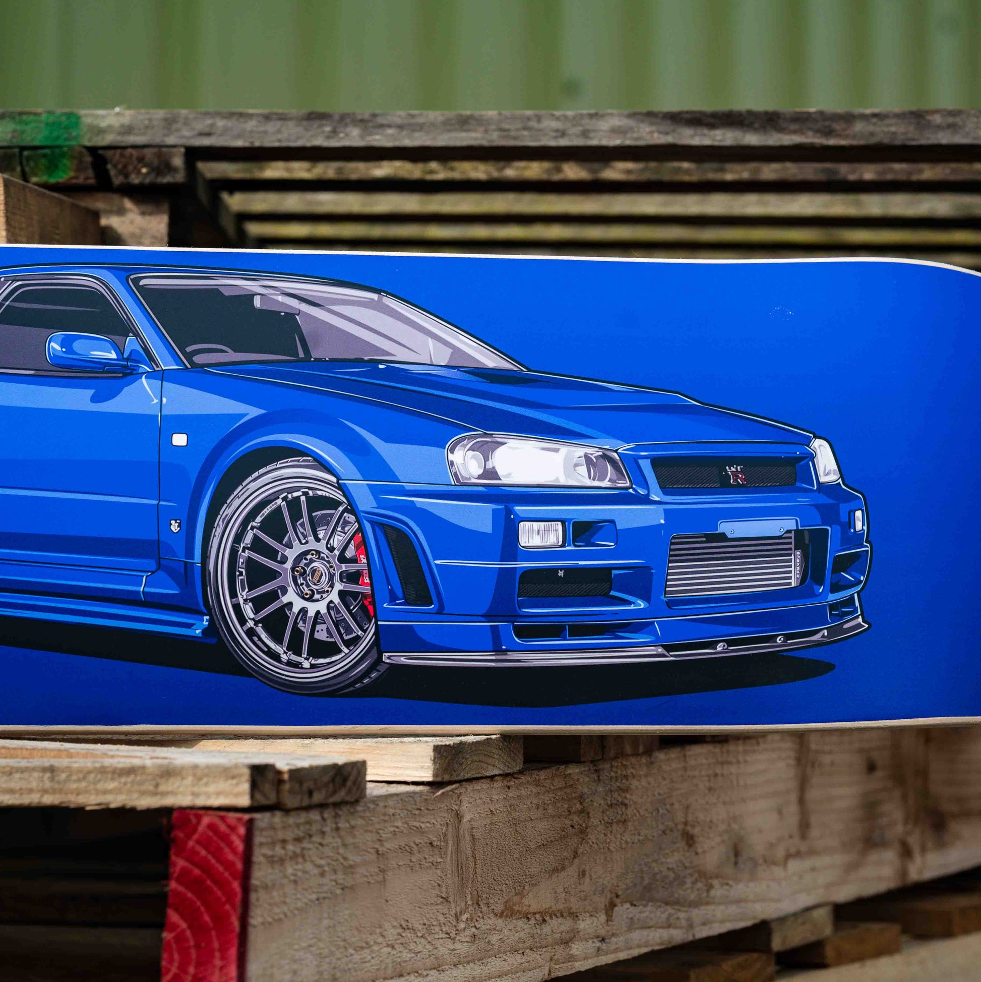 Blue car on a wooden pallet with a green container in the background