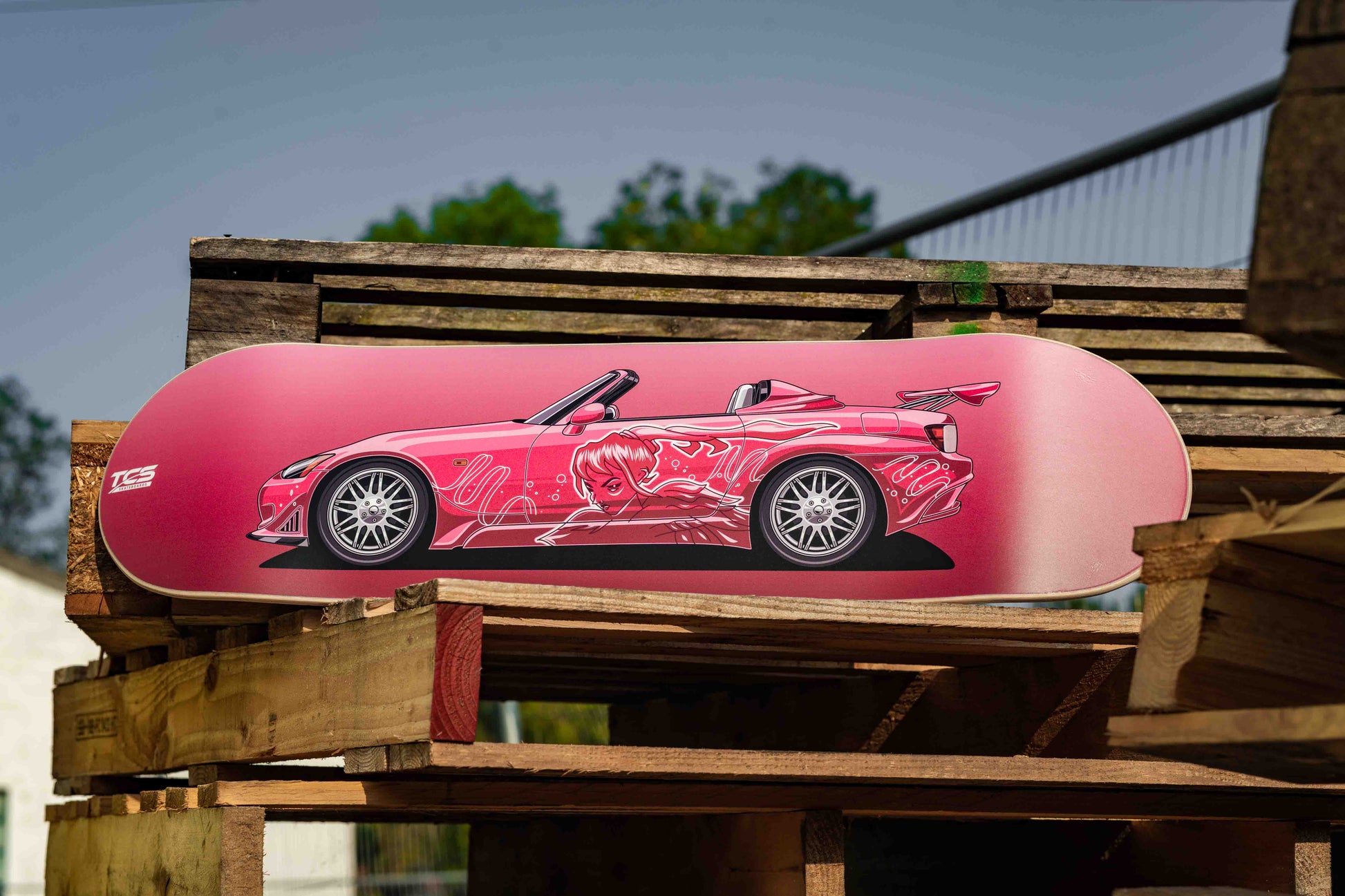 Pink sports car model on wooden pallets with a blurred outdoor background