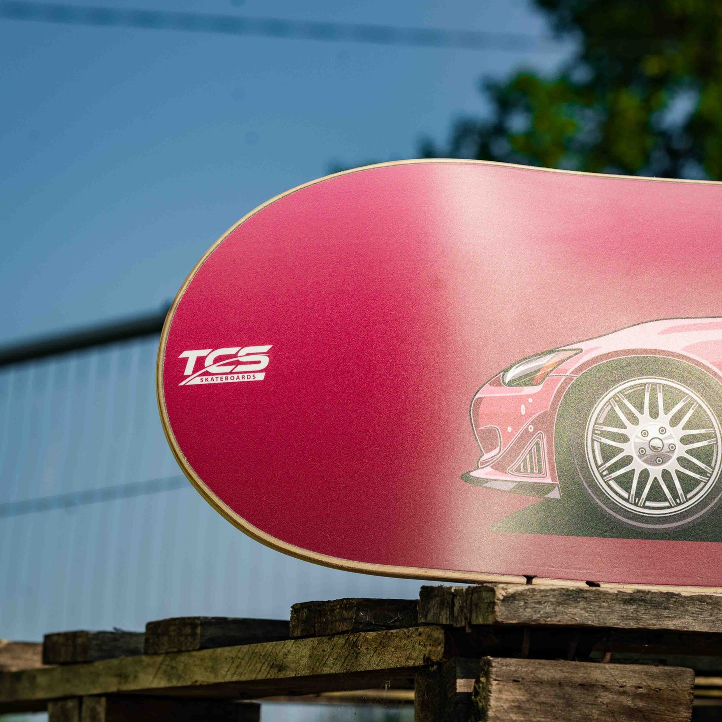 Red skateboard deck with a car graphic and 'TCS' branding on a wooden surface.