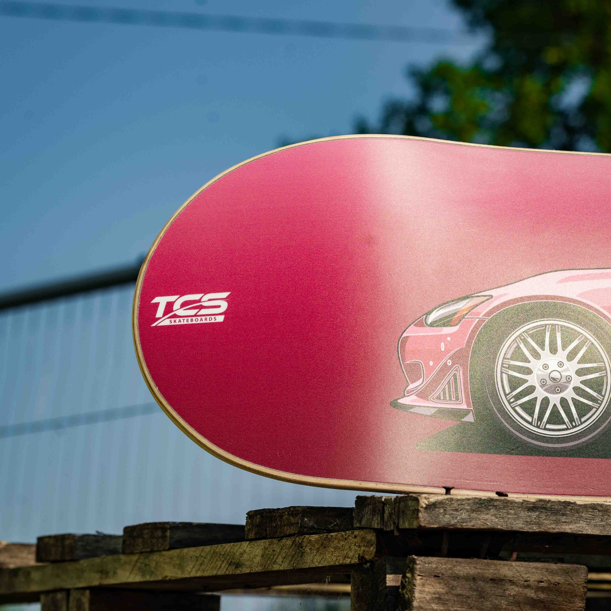 Red skateboard deck with a car graphic and 'TCS' branding on a wooden surface.