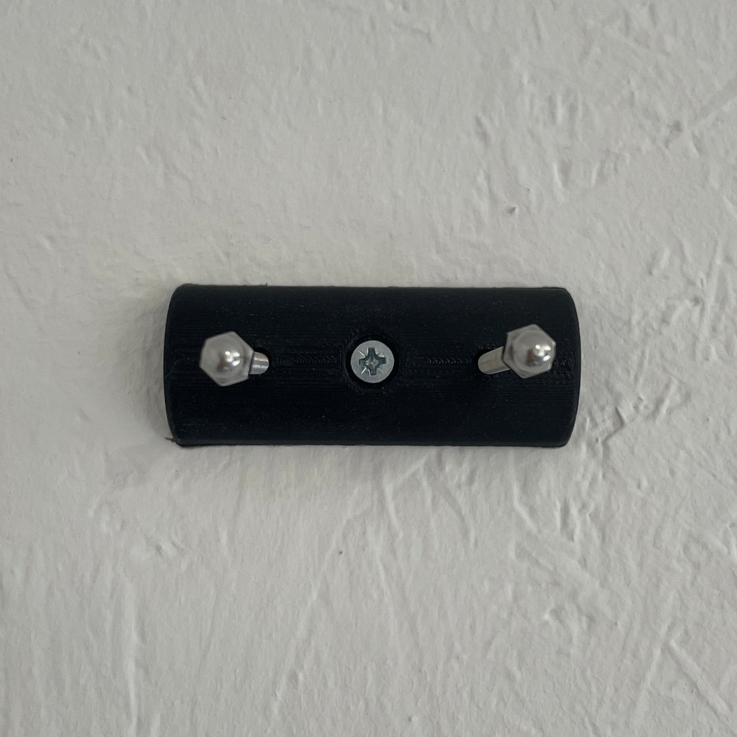 Black wall-mounted device with screws on a textured light gray wall