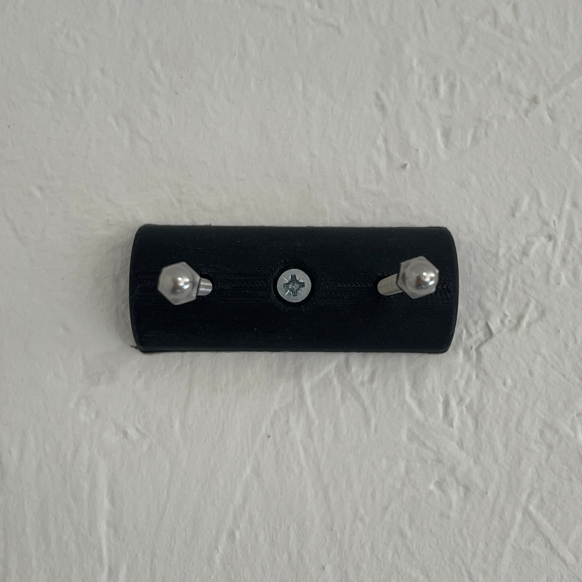 Black wall-mounted device with screws on a textured light gray wall