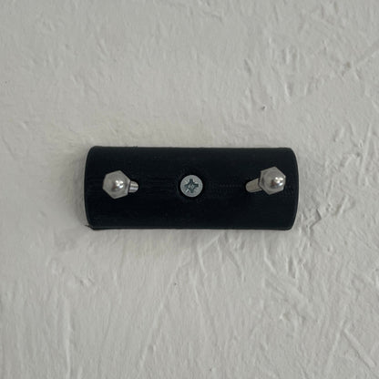 Black wall-mounted device with screws on a textured light gray wall