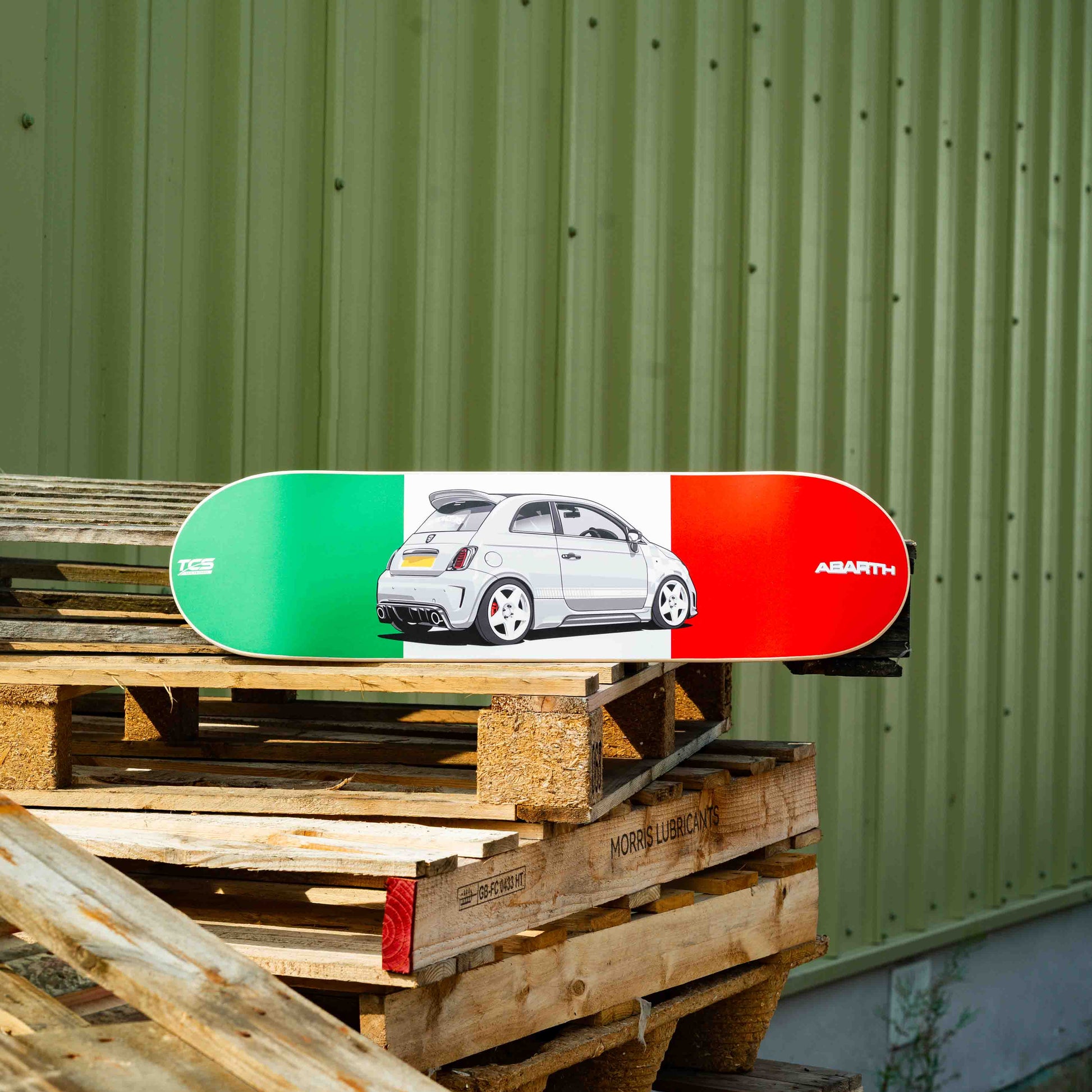 Skateboard with a car design on a wooden pallet against a green wall.
