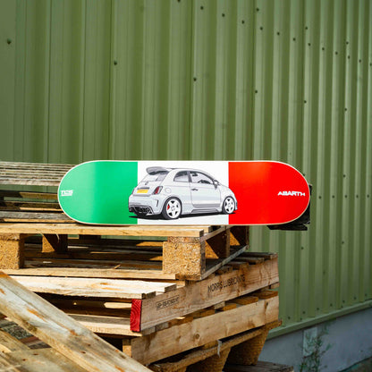 Skateboard with a car design on a wooden pallet against a green wall.