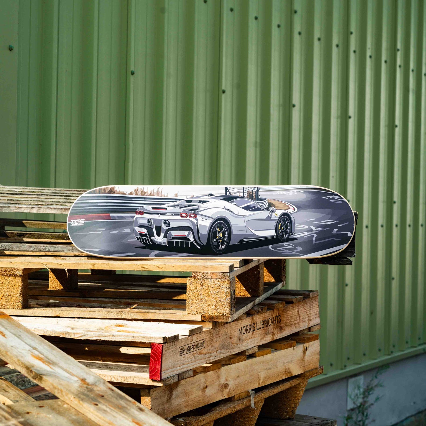 Skateboard with a car design on top of wooden pallets against a green wall.