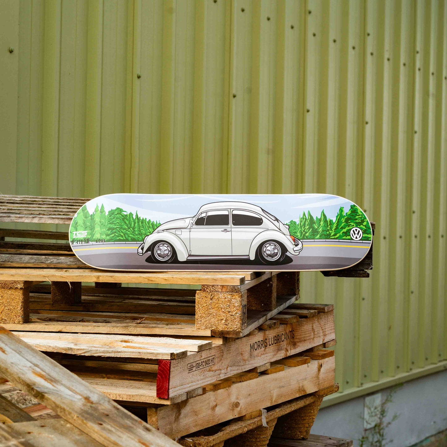 Skateboard deck with a car design on wooden pallets against a green wall.