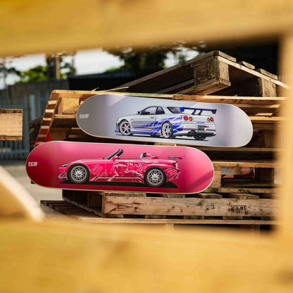 Two skateboard decks with car designs on a wooden pallet outdoors.