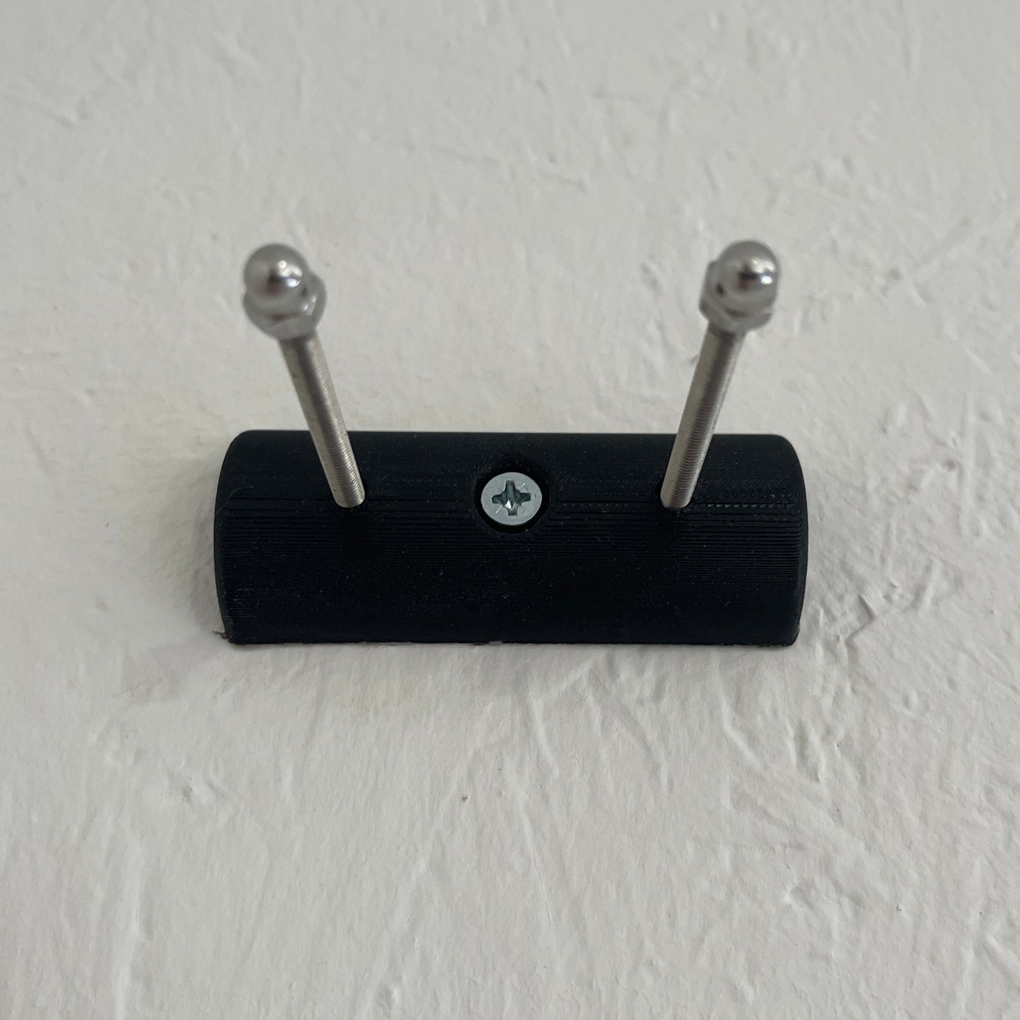 Black wall-mounted hook with two silver hooks on a light gray wall.