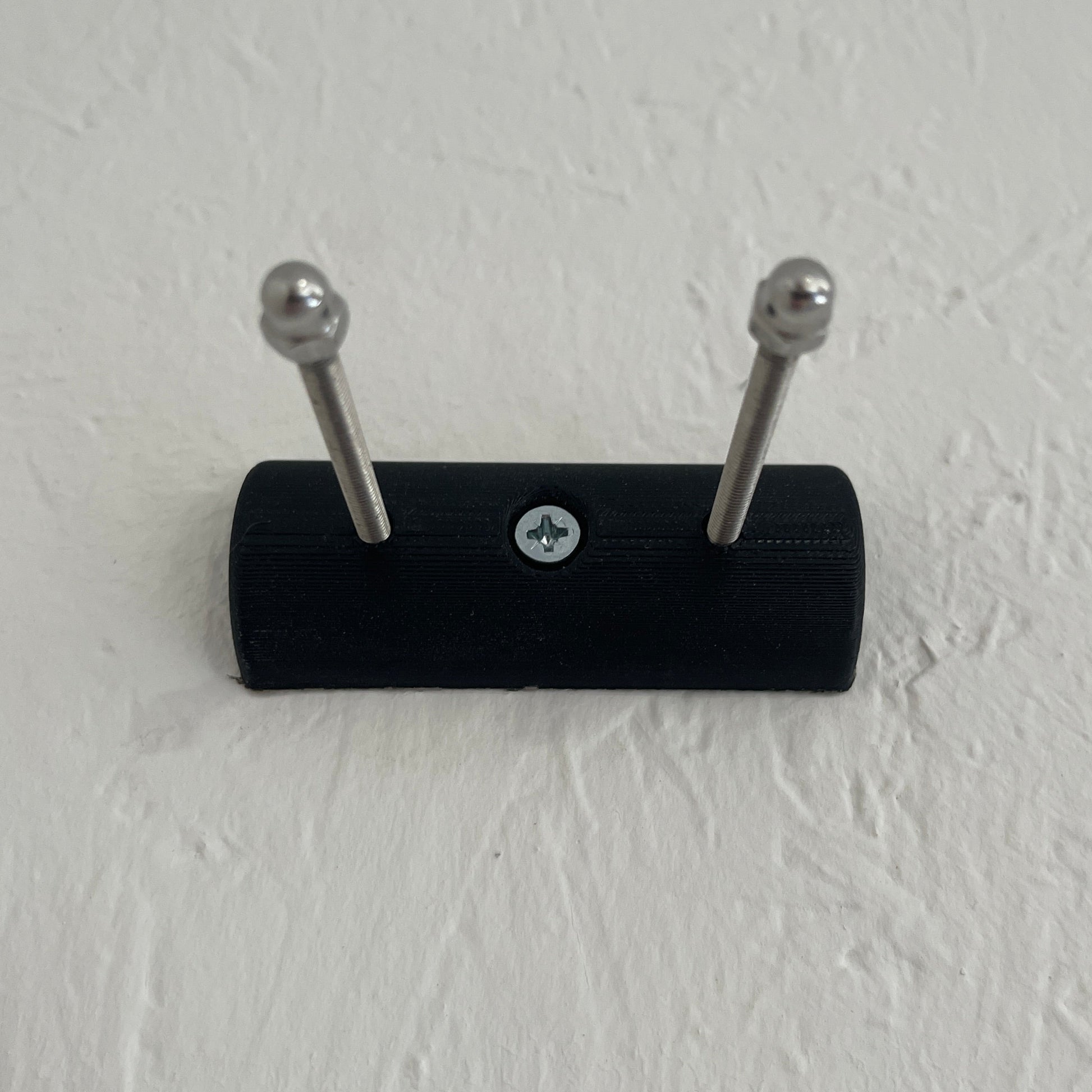 Black wall-mounted hook with two silver hooks on a light gray wall.