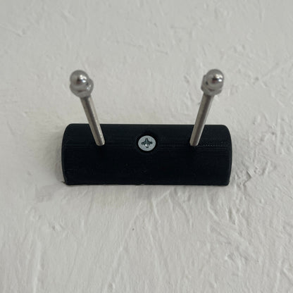 Black wall-mounted hook with two silver hooks on a light gray wall.