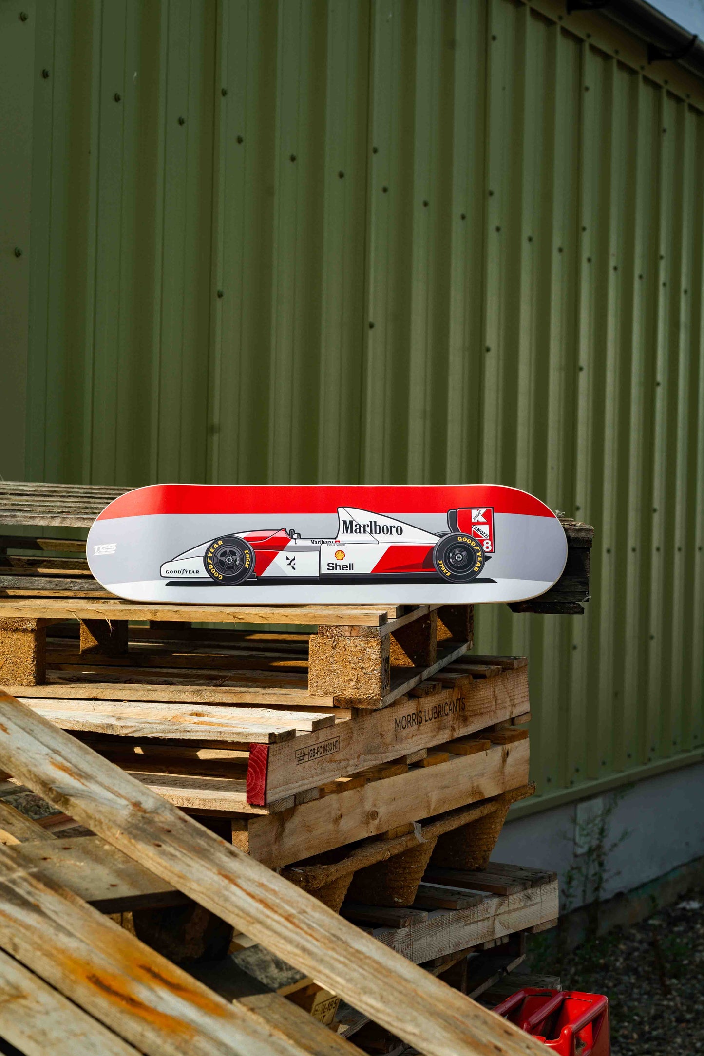 Red and white skateboard deck on wooden pallets with a green corrugated metal background