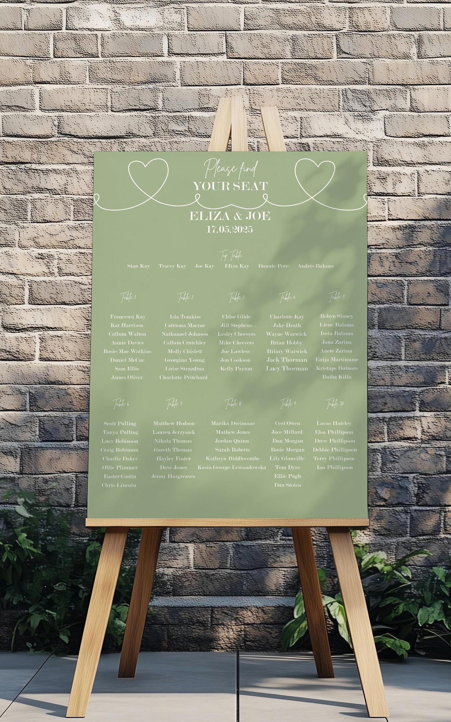 Green wedding seating chart on a wooden easel against a brick wall.