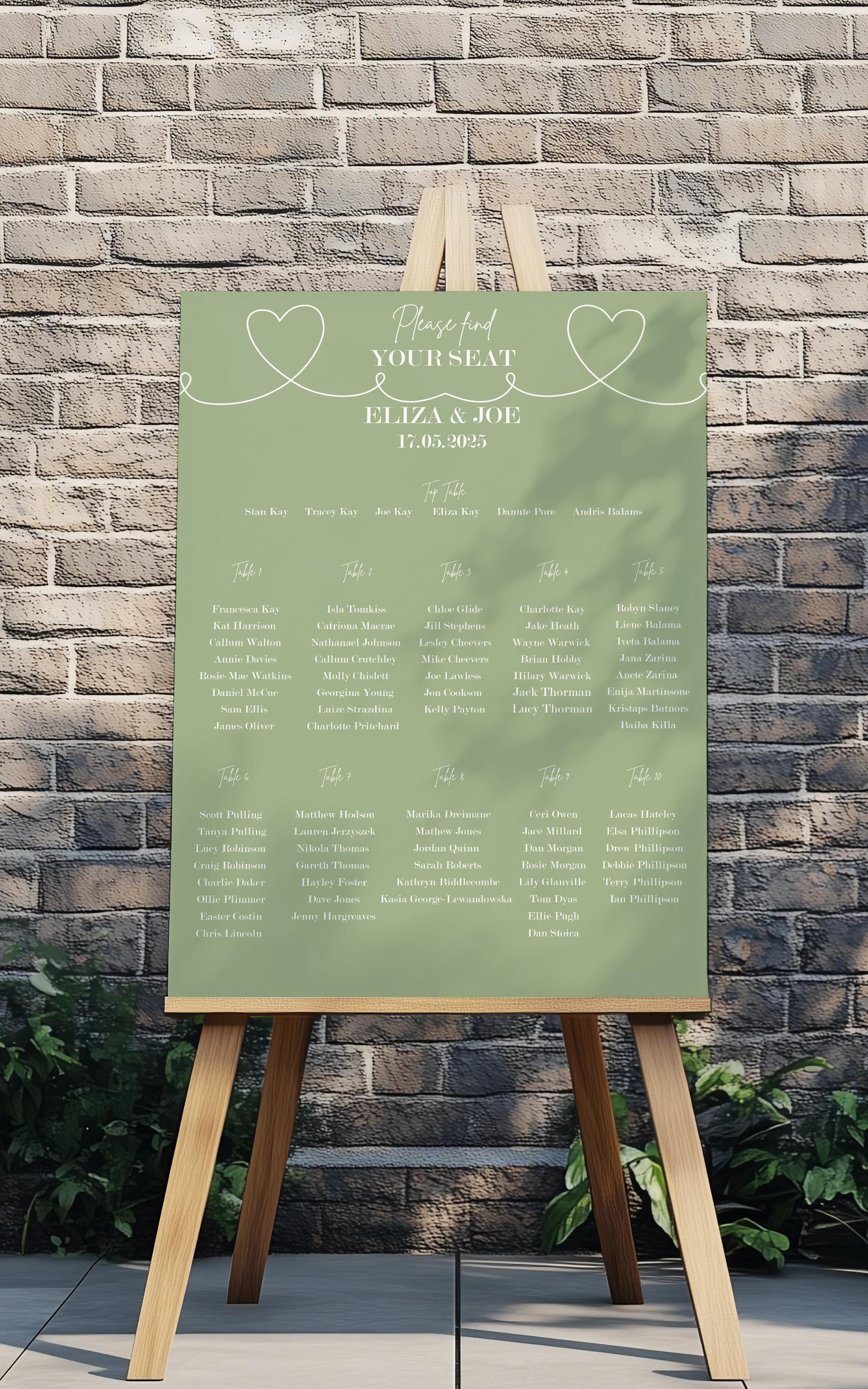 Green wedding seating chart on a wooden easel against a brick wall.